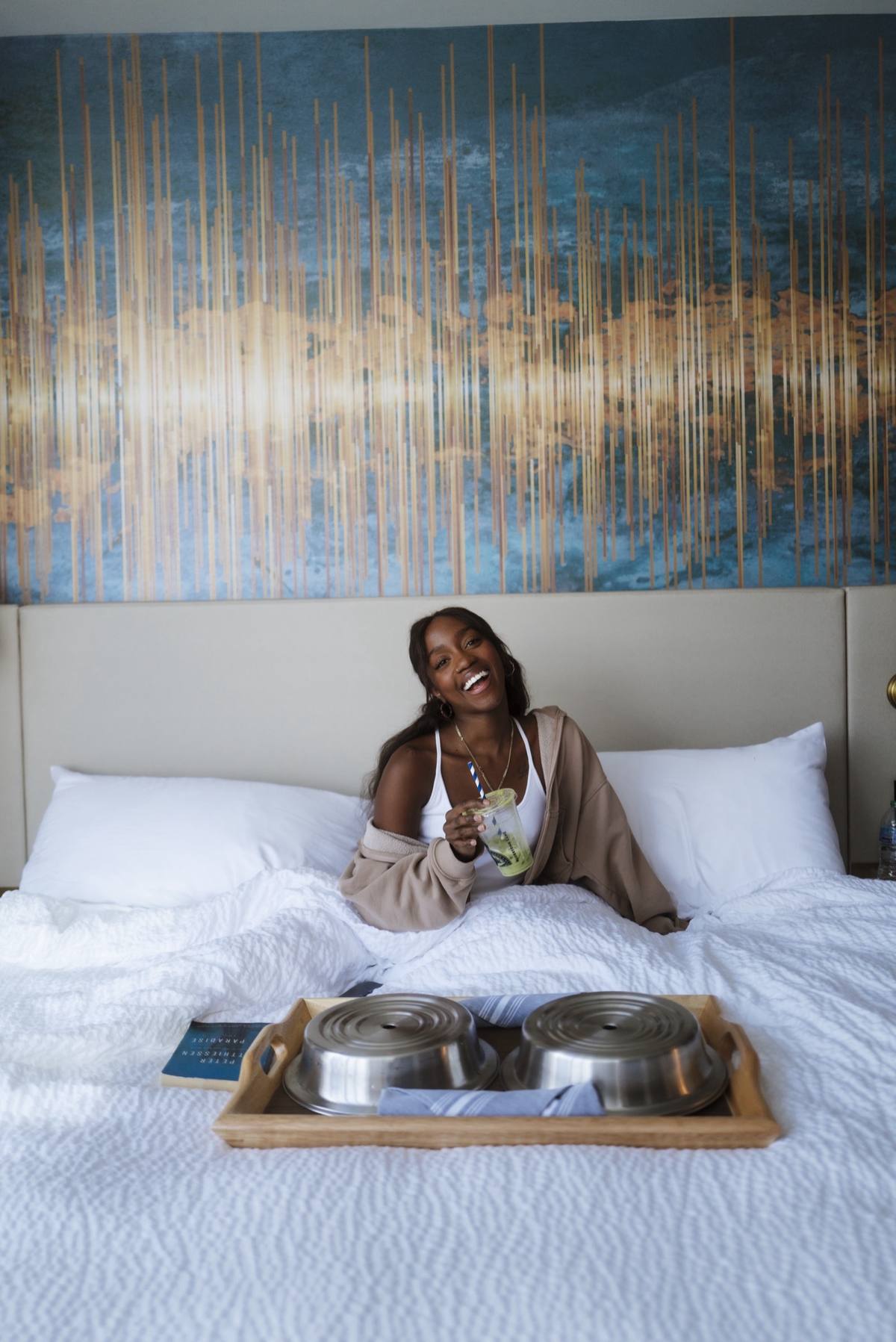 Hotel guest smiling in bed with an in-room breakfast tray, an authentic lifestyle moment rather than a staged empty room