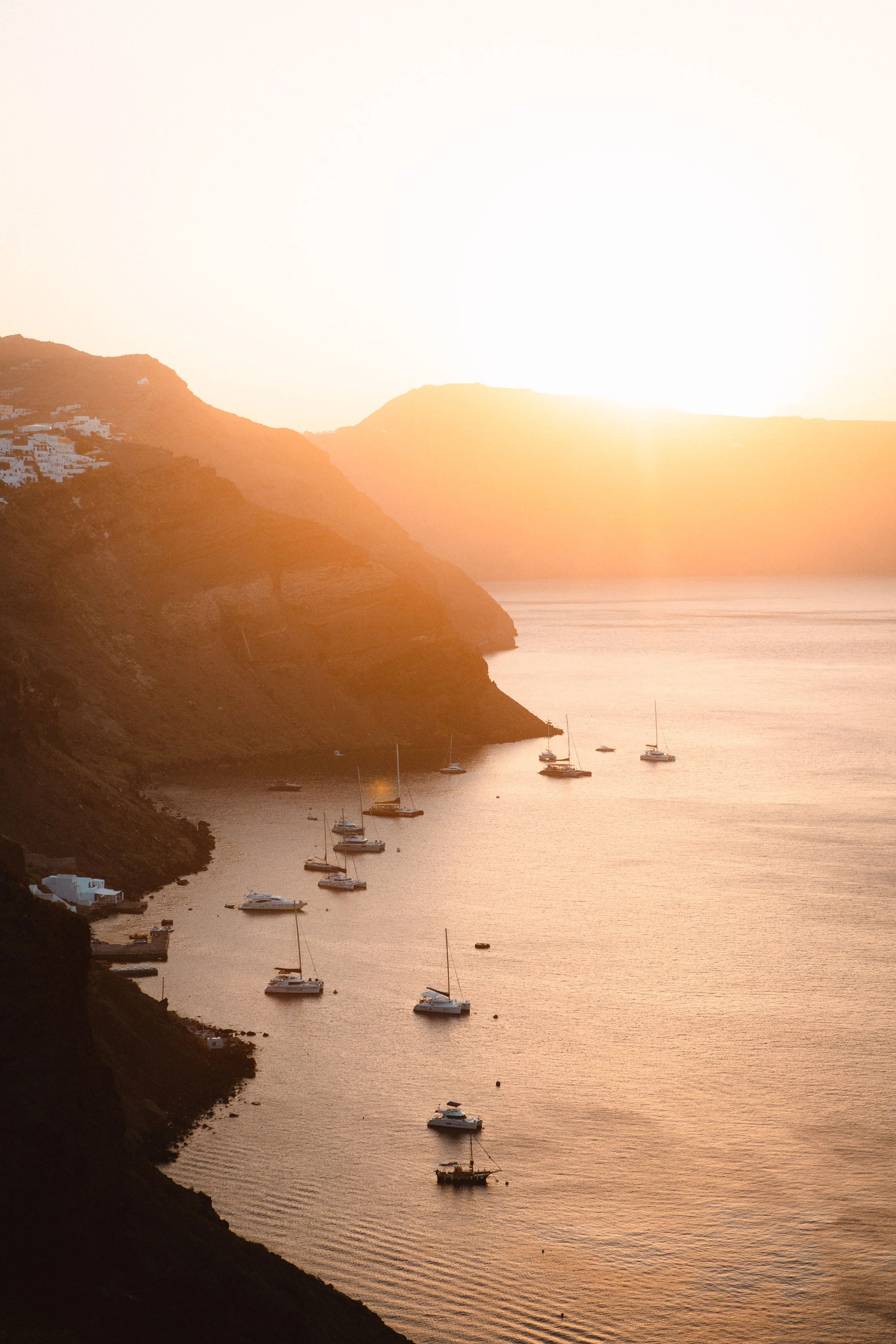 Golden hour view of Santorini's caldera coastline with anchored sailboats and yachts