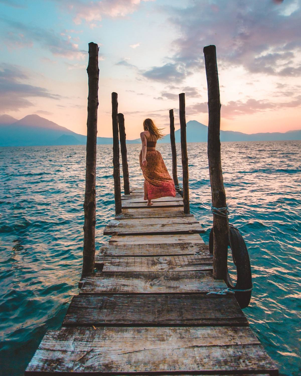 Traveler walking along a wooden dock at sunset with mountains in the distance