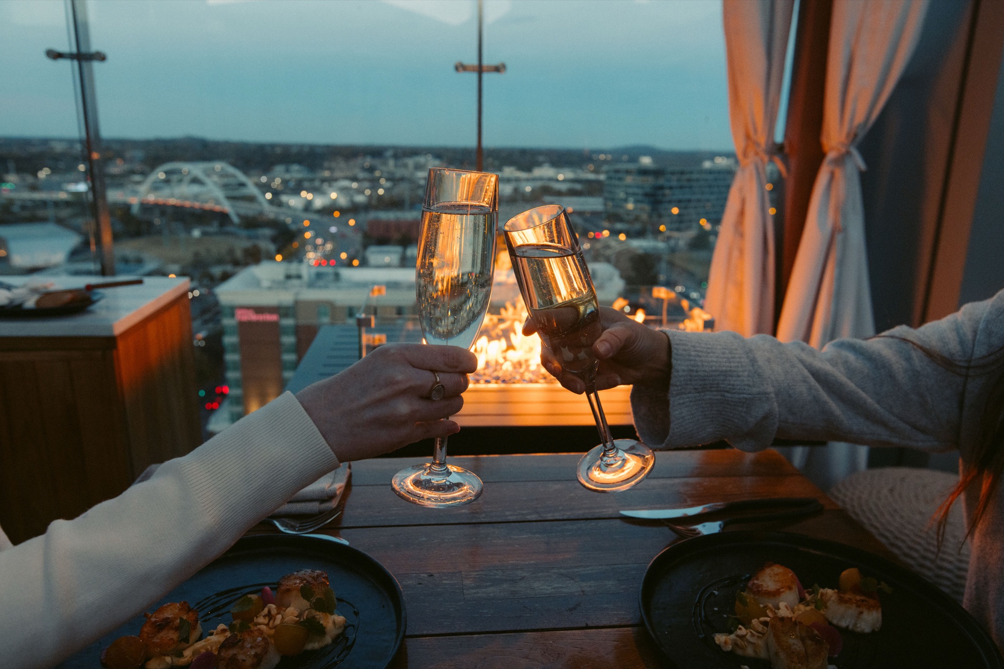 Couple toasting champagne on a rooftop restaurant terrace overlooking the Nashville skyline at dusk