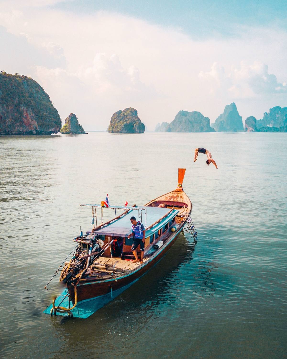 Traveler performing a backflip off a longtail boat near limestone islands