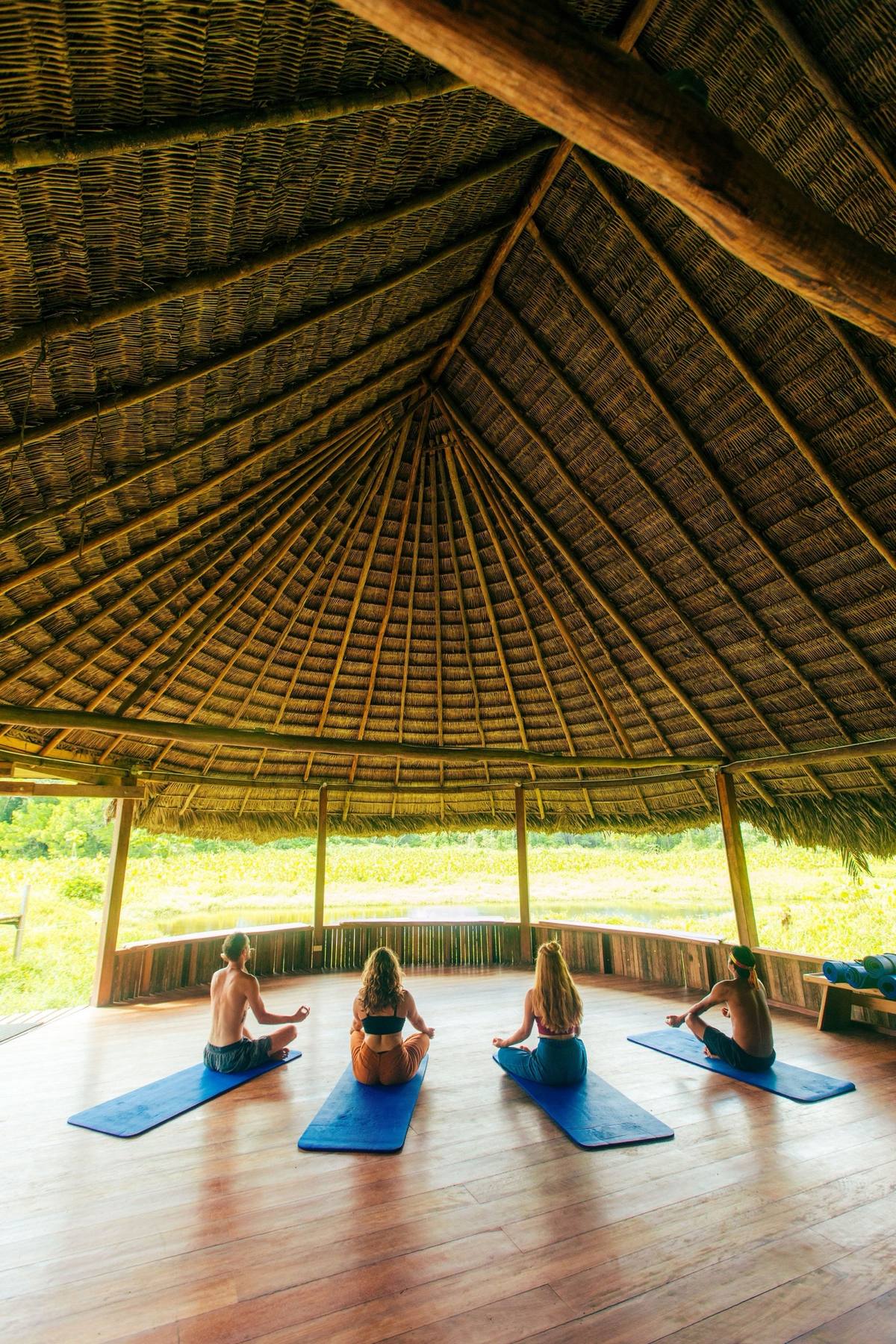 Guests practicing yoga under a thatched-roof pavilion at an Amazon ecolodge