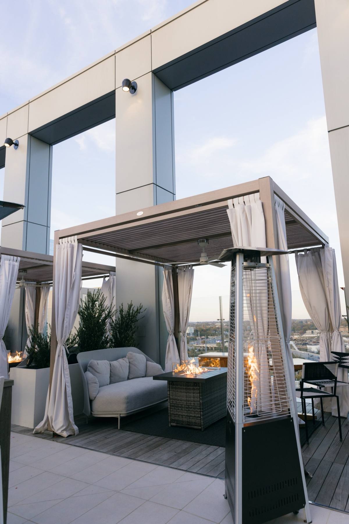 Modern rooftop lounge with cabanas and a fire feature overlooking a city skyline